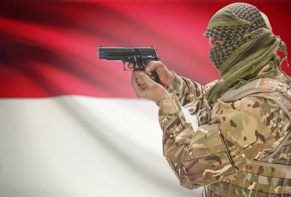 Male in muslim keffiyeh with gun in hand and national flag on background - Indonesia