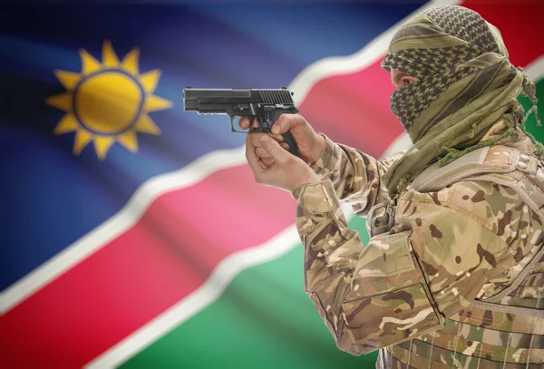 Male in muslim keffiyeh with gun in hand and national flag on background - Namibia