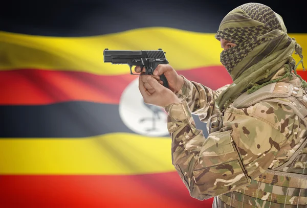 Male in muslim keffiyeh with gun in hand and national flag on background - Uganda