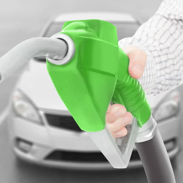 Green color fuel pump gun in hand with car on background - studio shot