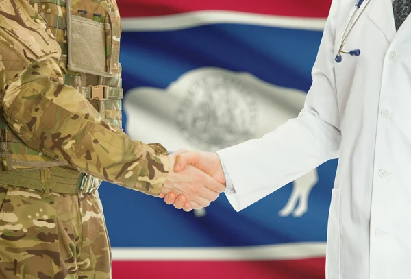 Military man in uniform and doctor shaking hands with US states flags on background - Wyoming