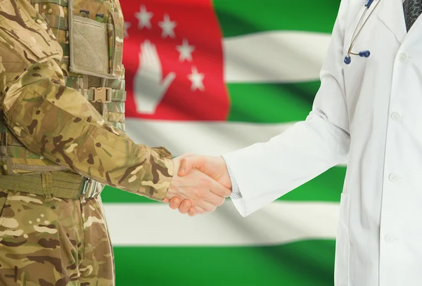 Military man in uniform and doctor shaking hands with national flag on background - Abkhazia