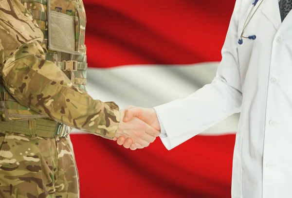 Military man in uniform and doctor shaking hands with national flag on background - Austria