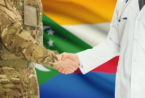 Military man in uniform and doctor shaking hands with national flag on background - Comoros