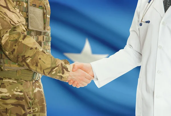 Military man in uniform and doctor shaking hands with national flag on background - Somalia