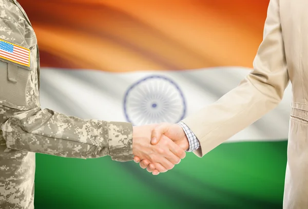 USA military man in uniform and civil man in suit shaking hands with national flag on background - India