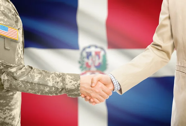 USA military man in uniform and civil man in suit shaking hands with national flag on background - Dominican Republic