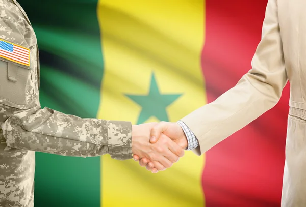 USA military man in uniform and civil man in suit shaking hands with national flag on background - Senegal