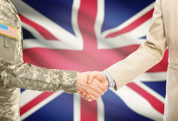 USA military man in uniform and civil man in suit shaking hands with national flag on background - United Kingdom