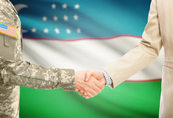 USA military man in uniform and civil man in suit shaking hands with national flag on background - Uzbekistan