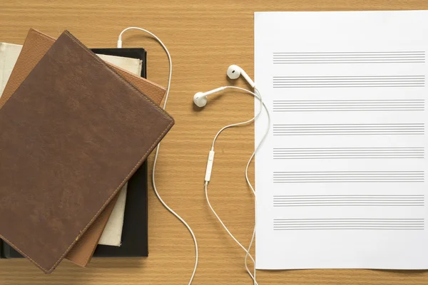 Top view of stack of notebook with earphone and music staff pape