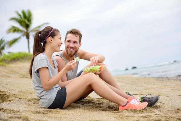 Fitness couple eating food sitting on beach