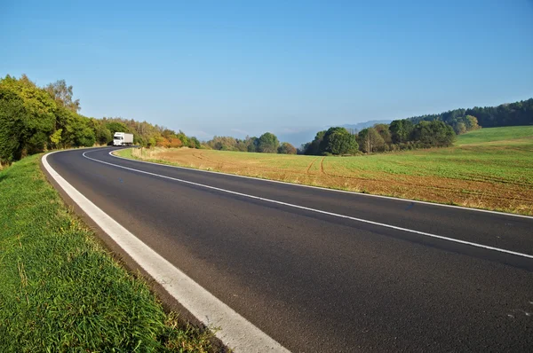 Asphalt road in the countryside, white truck coming around in the distance the bend