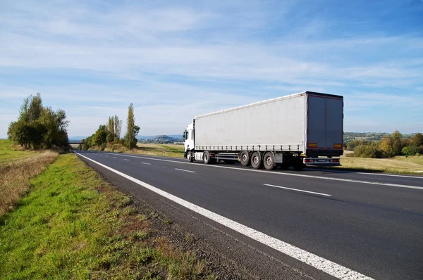 White truck travels on the asphalt road in the countryside.