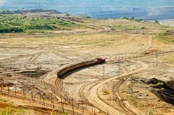Open-pit mine, mining train carrying excavated materials. Mining machines in the background.