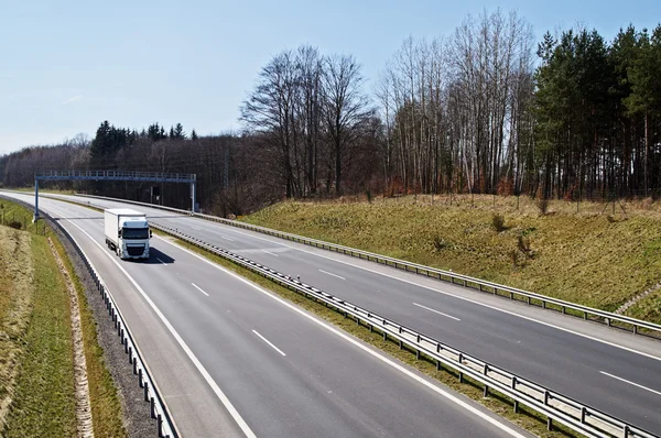 Motorway around the woods in early spring. White truck under electronic toll gates.