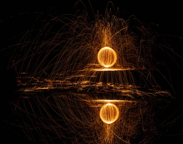 Fire ball of spinning hot steel wool and water reflection