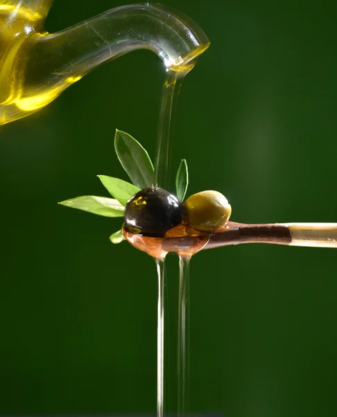 Olive oil falling on two olive with olive leaves