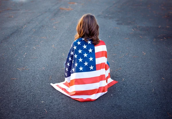Sad lonely patriot woman sitting down with the american flag wra