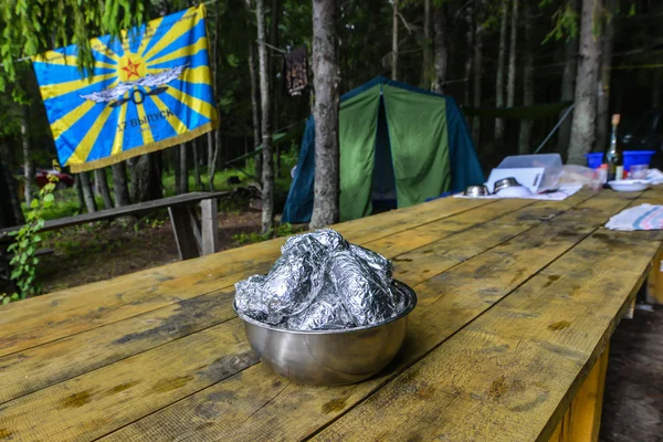 LAKE SELIGER, RUSSIA - CIRCA JUNE 2015: wooden table with a bowl of potatoes in foil at the picnic area circa June 2015.