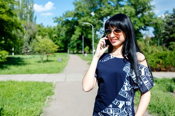 Beautiful brunette girl speaks by phone in the park