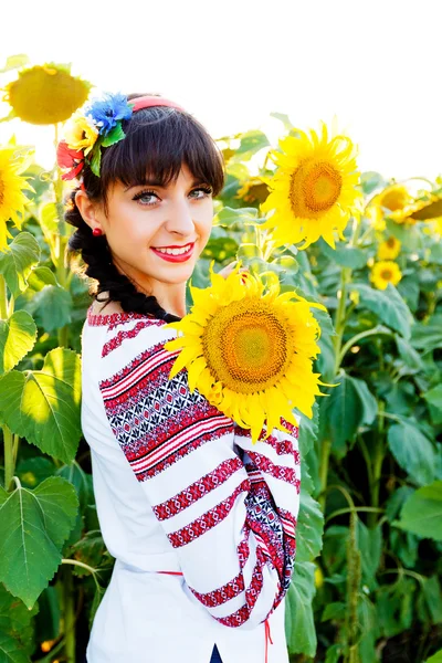 Beautiful young girl in embrodery holding a sunflower on a  plan