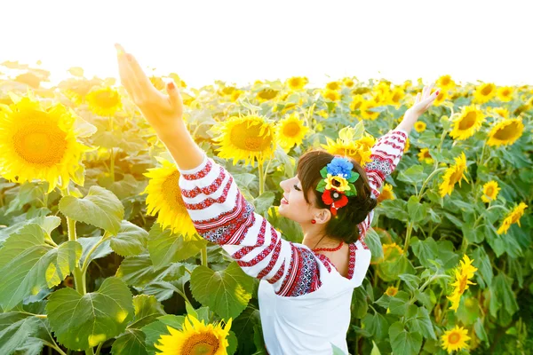 Beautiful girl in embrodery rise hands up on a sunflower plant