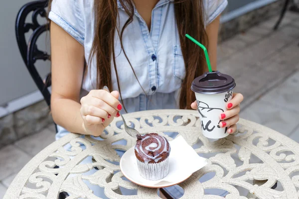 Young woman eating muffin and drink coffee in outdoors cafe