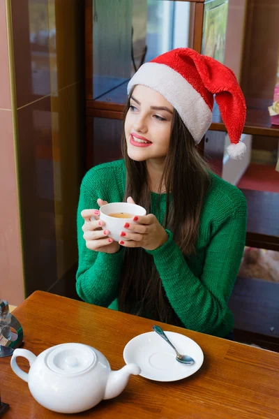Young beautiful woman in  Santas hat drinking tea in cafe