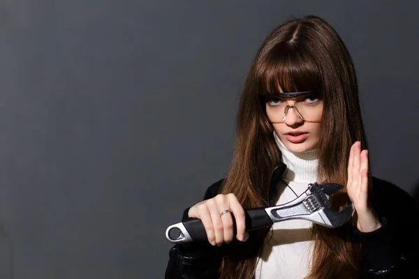 Girl in safety glasses with adjustable wrench on a dark backgrou