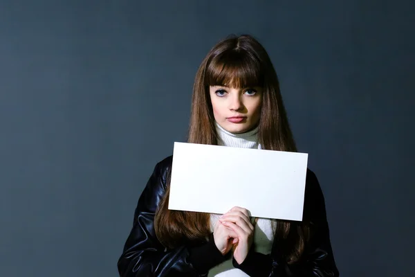 Girl with empty white blank card on a dark wall background