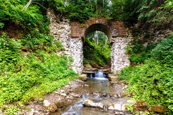 Mountain stream flows through the old stone archway in the fores
