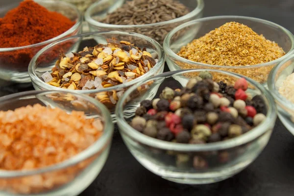 Various kinds of spices in glass bowls on a slate background. Preparation for cooking spicy food. Spices for master cook. The spice trade. Sale of spices in the kitchen.