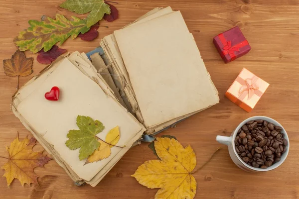 Dry leaves, old book and coffee on wooden background. Autumn romance. The book of romantic tales.