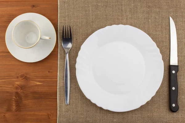 Empty white plate with knife and fork on a wooden table. Waiting for food. Home dining. Directly above view of table setting. Diet food.