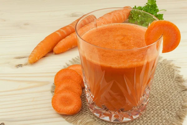 Glass of carrot juice and carrots on the wooden table. Healthy juice full of vitamins and fiber. Diet Food. Carrot segments on a wooden background.