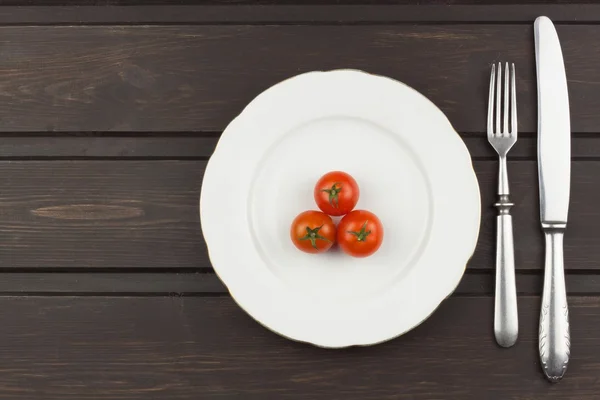 Very strict diet. Dietary vegetable diet. Tomatoes on a plate. Slimming diet. White plate with tomato on dark table.
