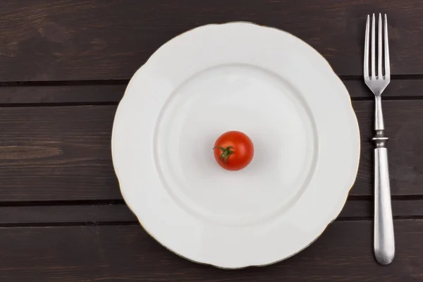 Very strict diet. Dietary vegetable diet. Tomatoes on a plate. Slimming diet. White plate with tomato on dark table.