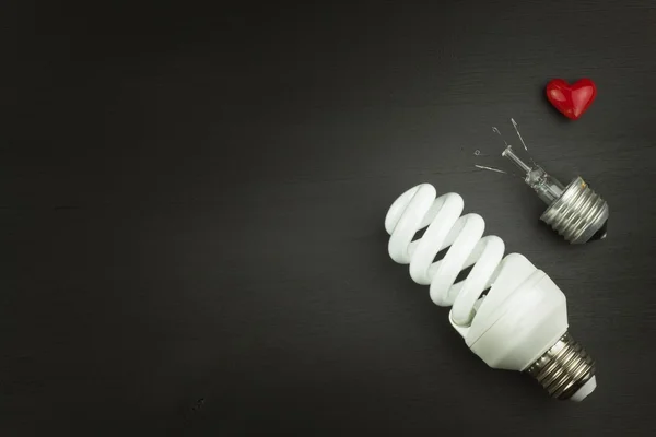 Energy saving lamp on black wooden background. Sales of light bulbs. Advertising for energy-saving bulbs. Place for your text.