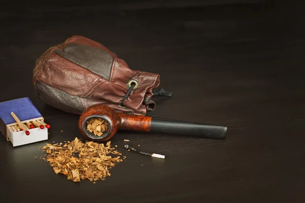 Old tobacco pipe and spilled tobacco, used on a black wooden background. Shabby old tobacco pipe. Wooden tobacco pipe on a black background. Relaxing with a tobacco pipe. Quiet place. Chain smoker.