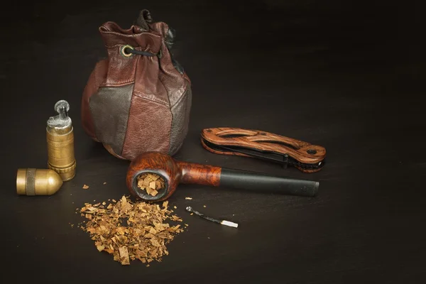 Old tobacco pipe and spilled tobacco, used on a black wooden background. Shabby old tobacco pipe. Wooden tobacco pipe on a black background. Relaxing with a tobacco pipe. Quiet place. Chain smoker.