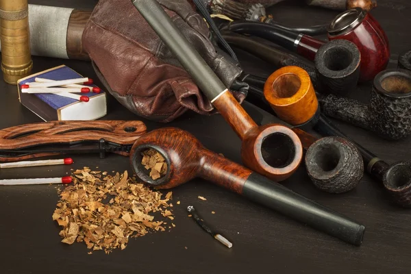 Old tobacco pipe and spilled tobacco, used on a black wooden background. Shabby old tobacco pipe. Wooden tobacco pipe on a black background. Relaxing with a tobacco pipe. Quiet place. Chain smoker.