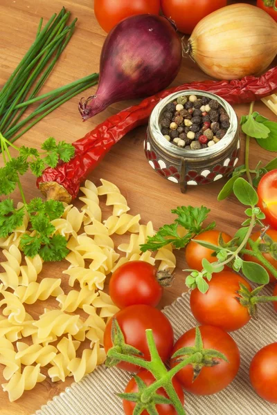 Raw pasta with tomatoes and parsley on a wooden background. Preparation diet food. The recipe for a simple dinner. Traditional pasta with vegetables.