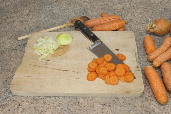 Slicing carrots on wooden cutting board, preparing vegetables for soup