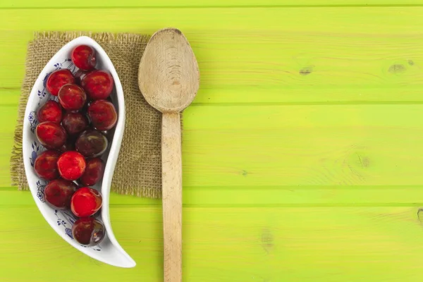 Cherries in a porcelain bowl on a green wooden table. Preparing for domestic production of marmalade. Background for creating menu.