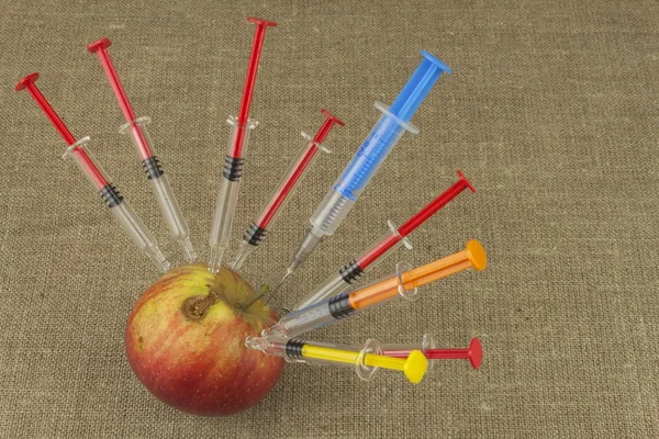 Genetic modification concept. Fruit and syginge. Apple receiving an injection of some substance for rapid ripening. Chemistry in the agricultural industry. Apple and syringe.