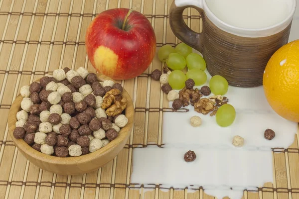 Spilled milk on the kitchen table. Chocolate cereal balls in a bowl of bamboo. Healthy breakfast with fruit and milk. A diet full of energy and fiber for athletes. Quick to prepare homemade breakfast.