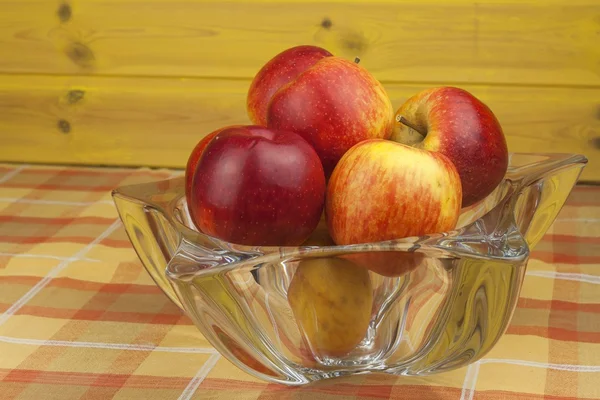 Red apples in a glass bowl on the kitchen table. Healthy food on the table. Autumn harvest of apples. Vitamins and fiber snack for children. Diet for athletes.