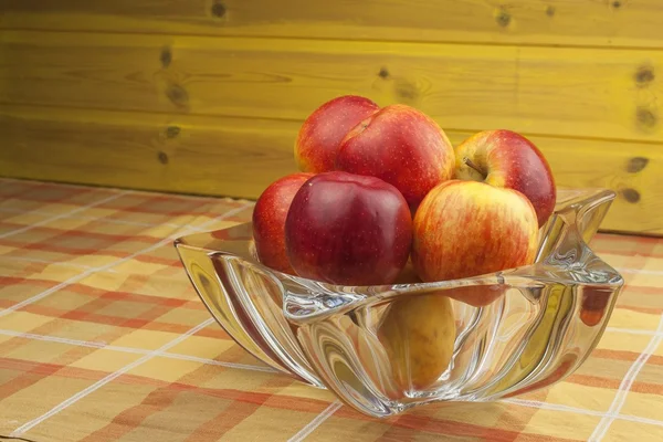 Red apples in a glass bowl on the kitchen table. Healthy food on the table. Autumn harvest of apples. Vitamins and fiber snack for children. Diet for athletes.