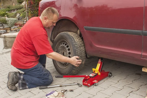 Man changing the punctured tyre on his car loosening the nuts with a wheel spanner before jacking up the vehicle. Repair flat tire on a passenger car. Replacing summer tires for winter tires.